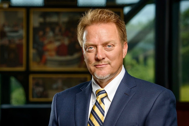 Dr. Gregory P. Seltz in a navy suit and gold striped tie